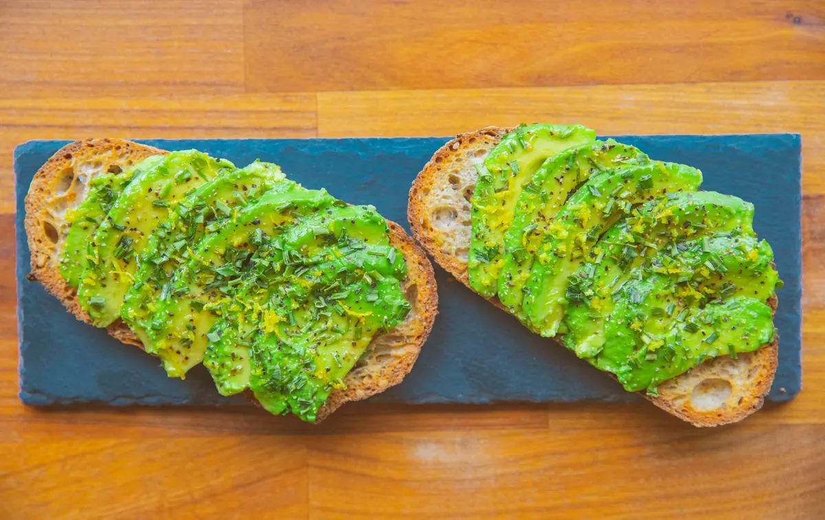 Two slices of avocado toast on a slate board