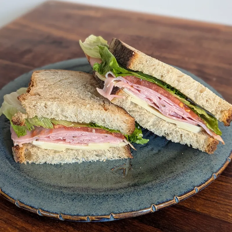Ham and cheddar sandwich on sourdough, cut in half on a blue plate