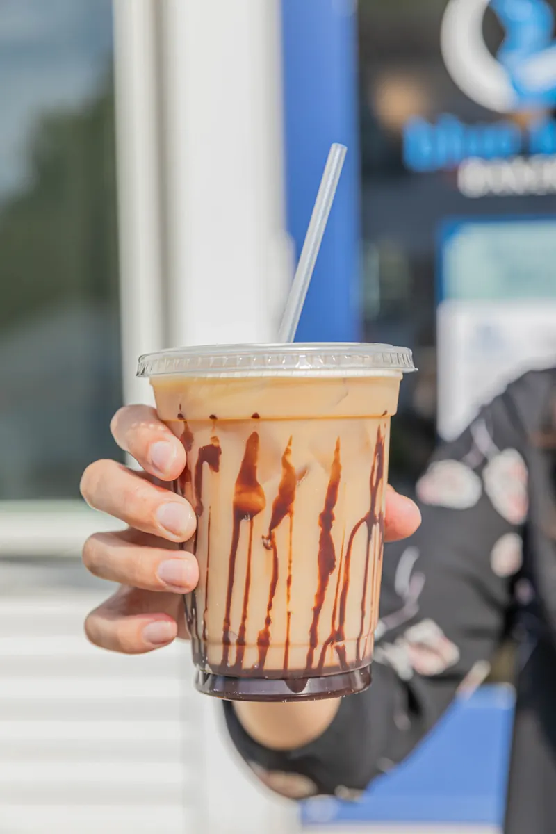 An iced mocha with chocolate drizzle held up outside the bakery