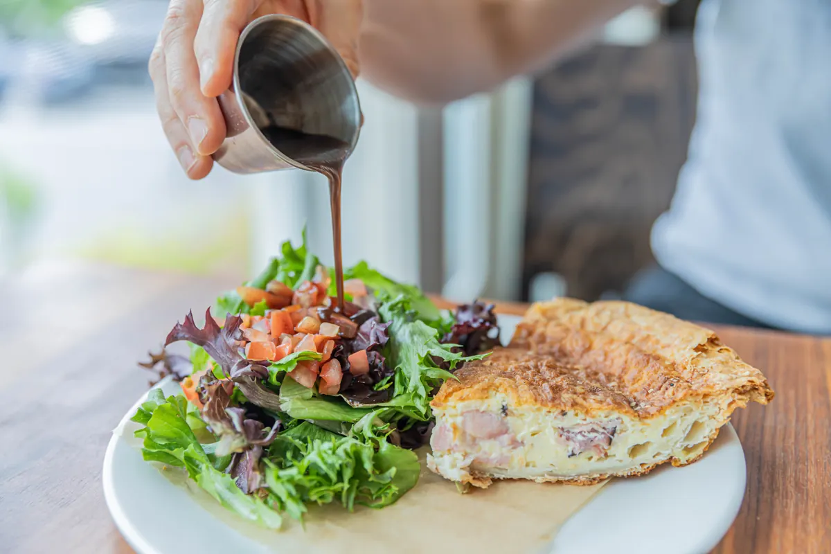 Dressing poured over a salad served with a slice of quiche