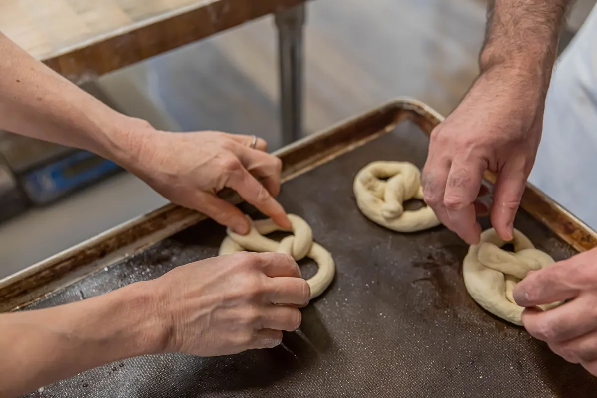 Bakers’ hands twisting pretzel dough on a baking sheet