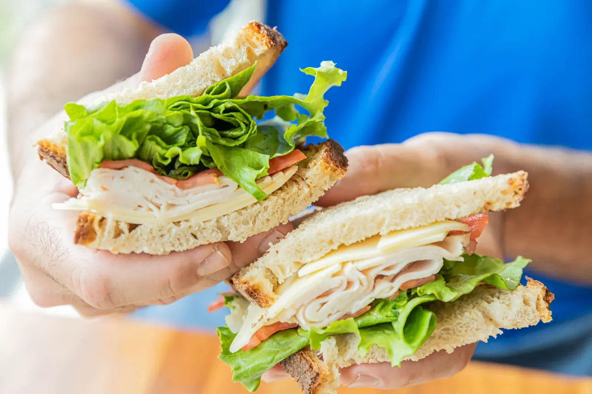 Hands holding a turkey sandwich with lettuce and tomato